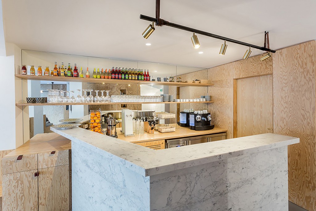 Rénovation de l'hôtel Montholon à Paris, livré en 2015. Il s'agit ici d'une photo du bar de l'hôtel. Les chambres ont été réaménagées autour d’une variation d’éléments en bois conçus et réalisés sur-mesure, tantôt dessinés comme un lit d’appoint ou une table, ou pour créer des panneaux et tablettes en tête de lit, des placards intégrés sur-mesure ou encore de grandes portes coulissantes toute hauteur donnant accès aux salles de bain. © TXKL